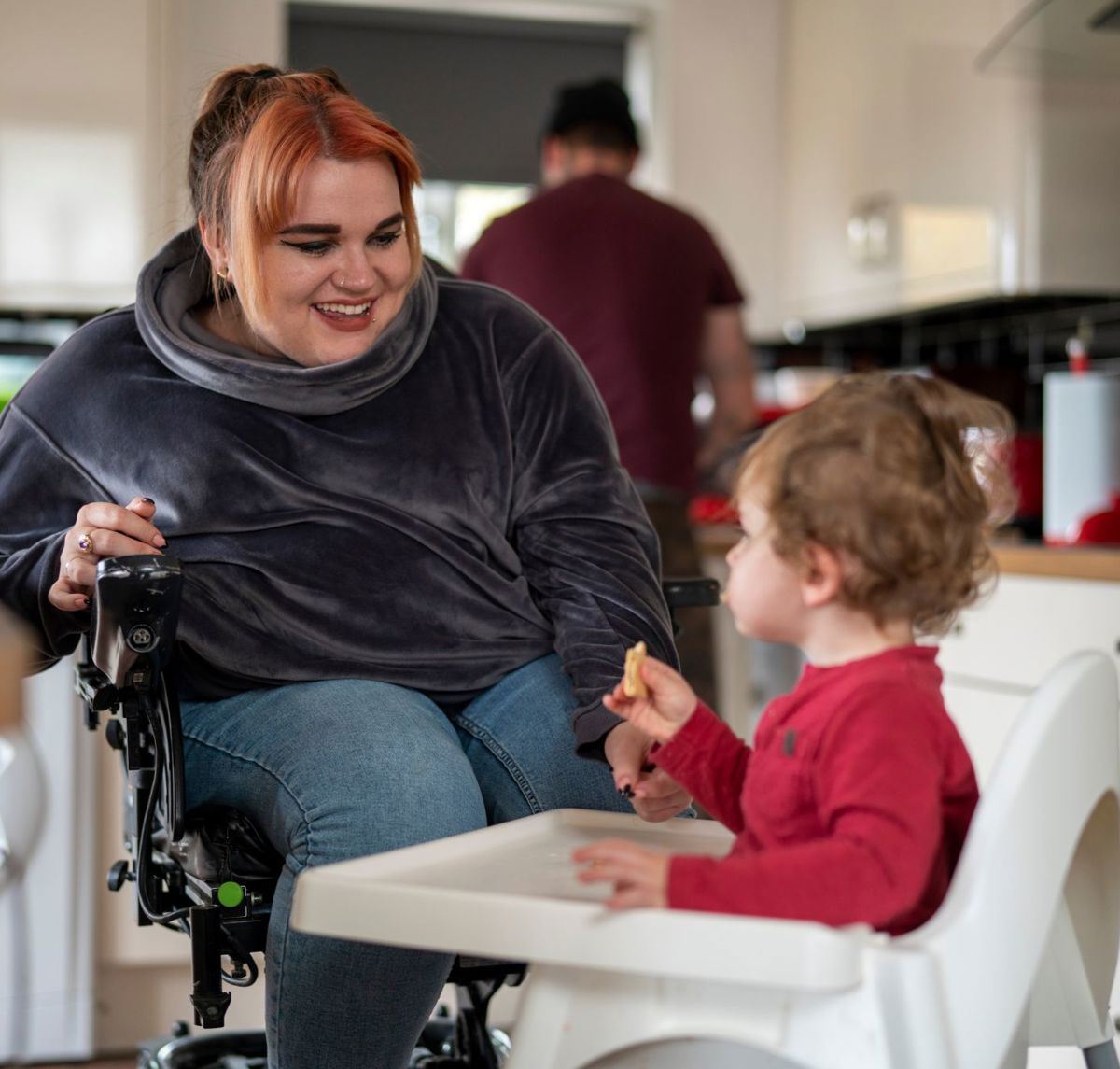 A disabled mother in a wheelchair feeding her son in his high chair in their kitchen