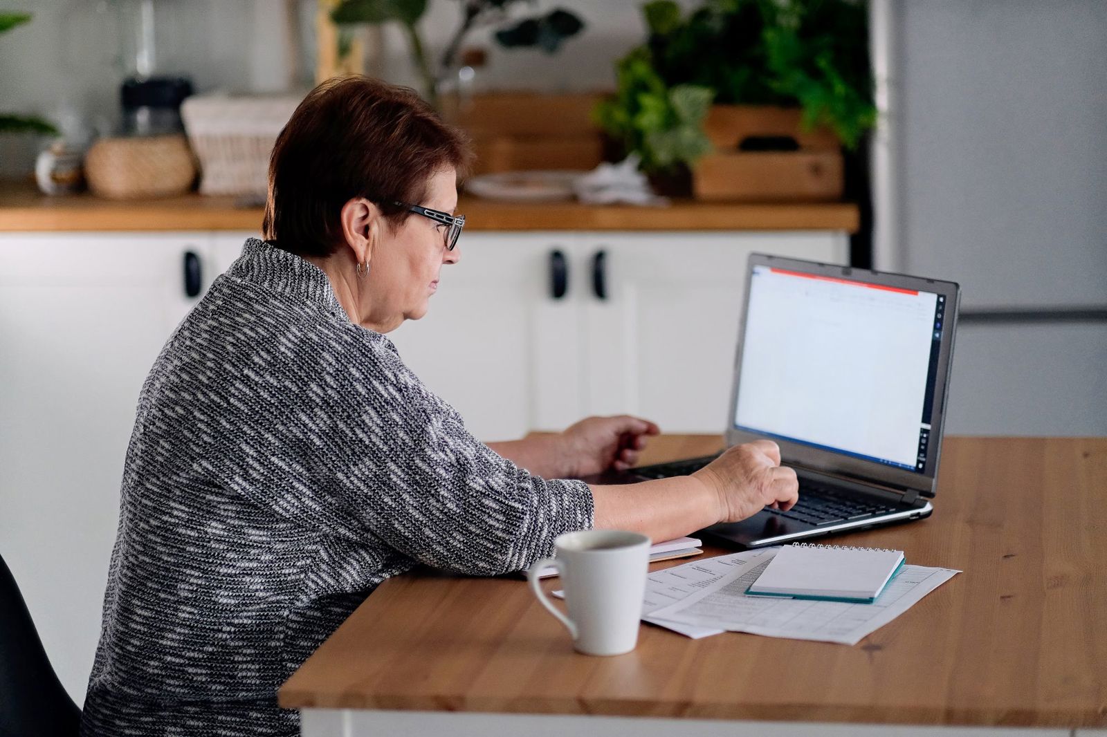 Older woman sat at her dining table using her laptop