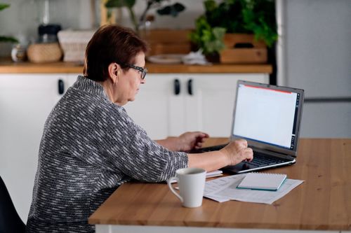 Older Woman Sat At Her Dining Room Table Using Her Laptop Stock