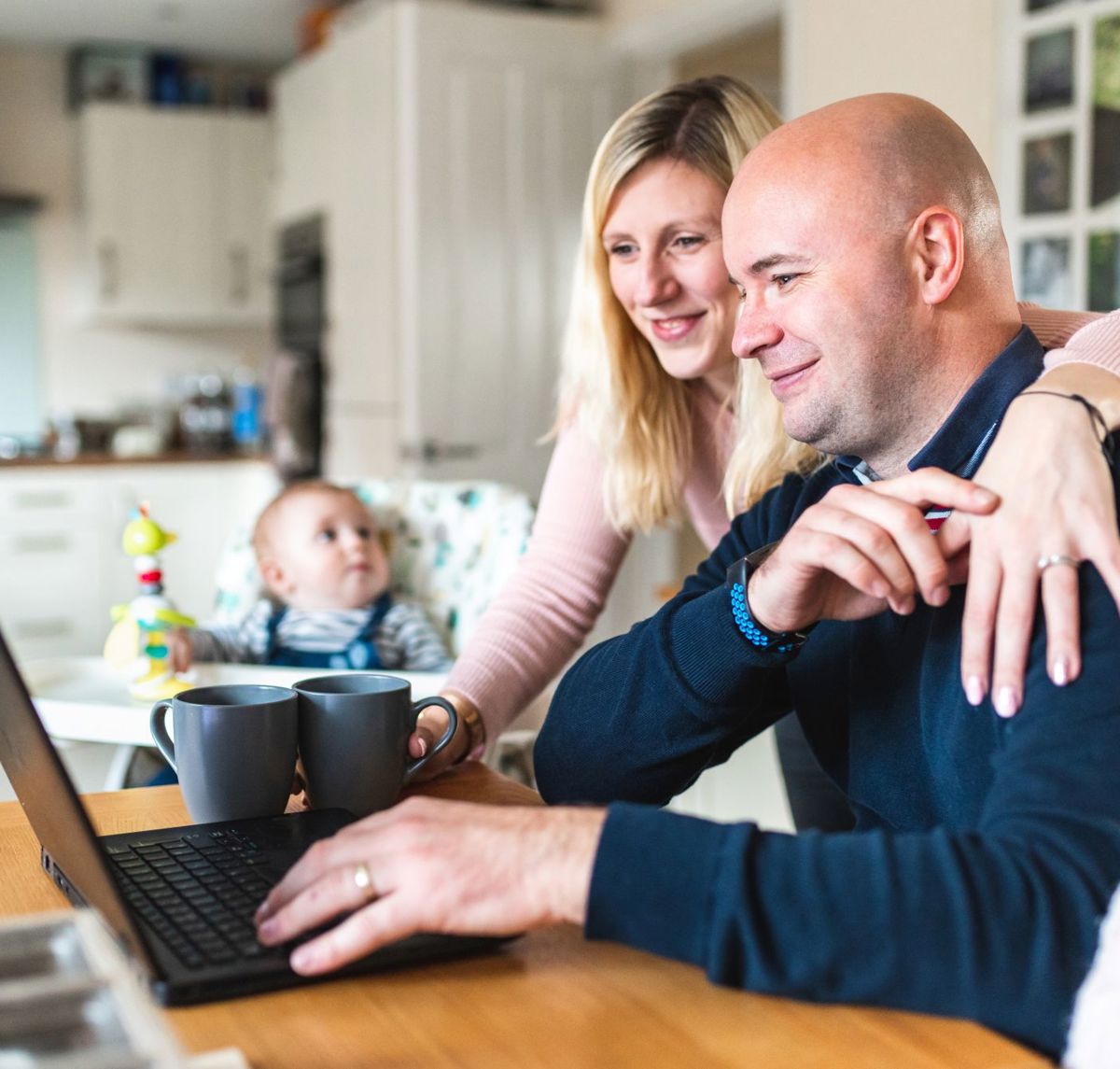 A Young Family At Their Dining Table Using A Laptop Stock