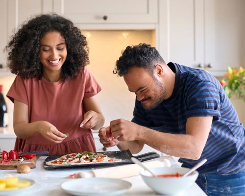 Man with Down Syndrome and woman putting toppings on a pizza in a kitchen together stock